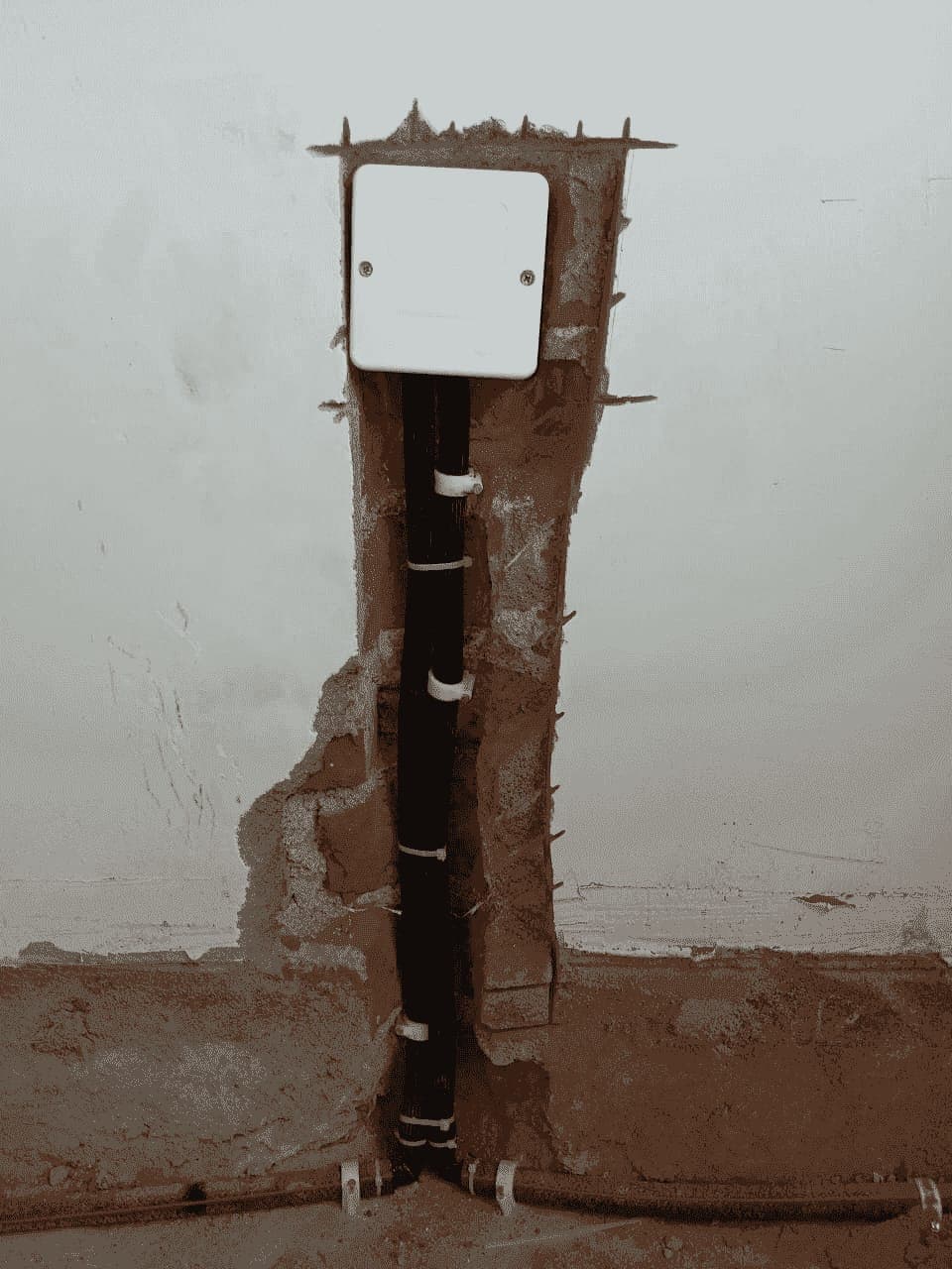 Wall-mounted injection box with anti-termite pipes running down a chase in the wall to floor level